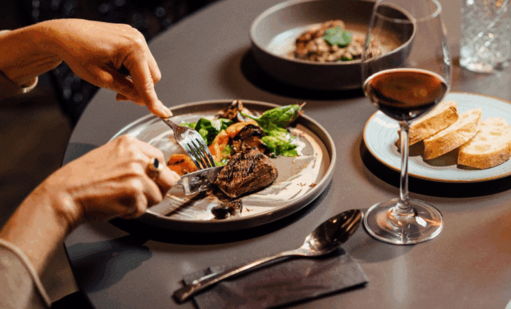 A person cutting a steak on a plate at a restaurant