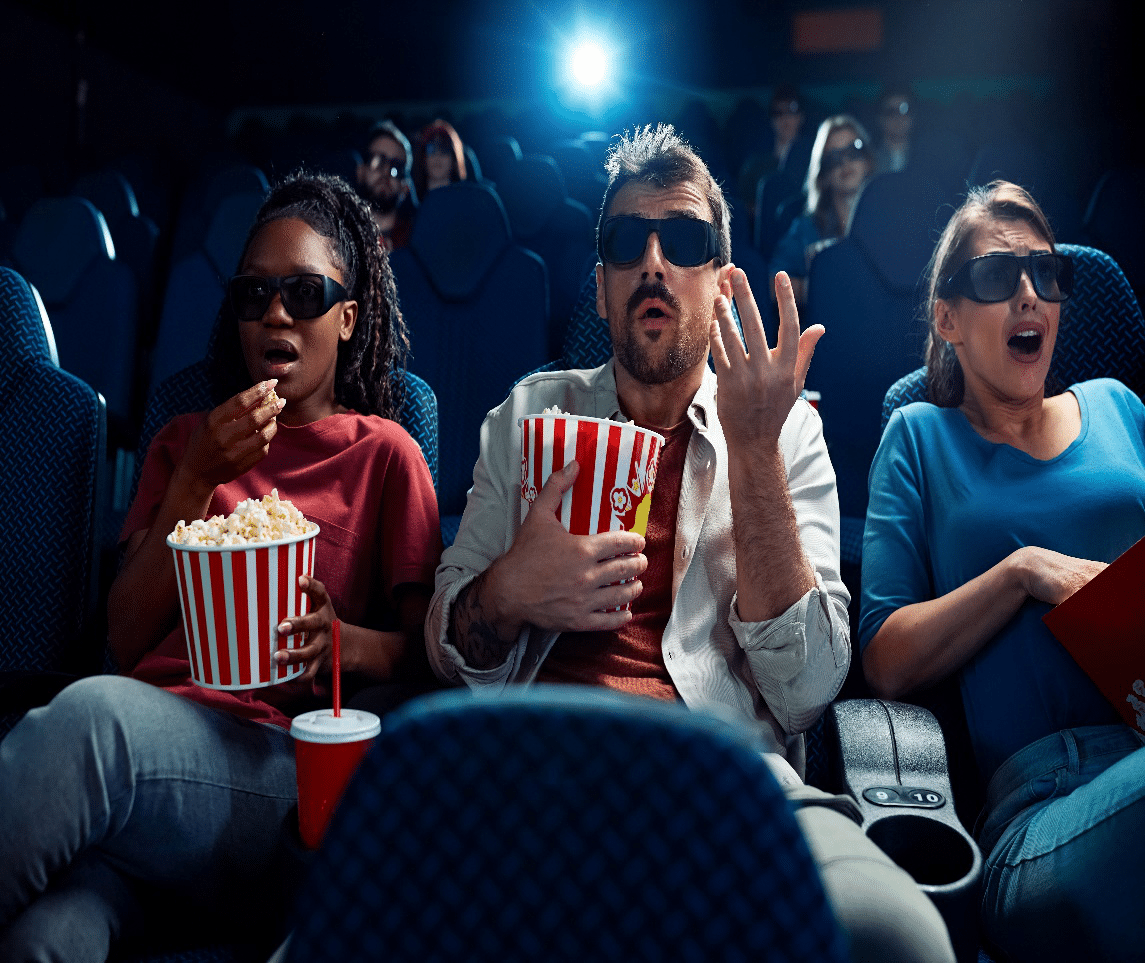 Group of friends wearing 3D glasses reacting to a suspenseful horror film in a dark theater.