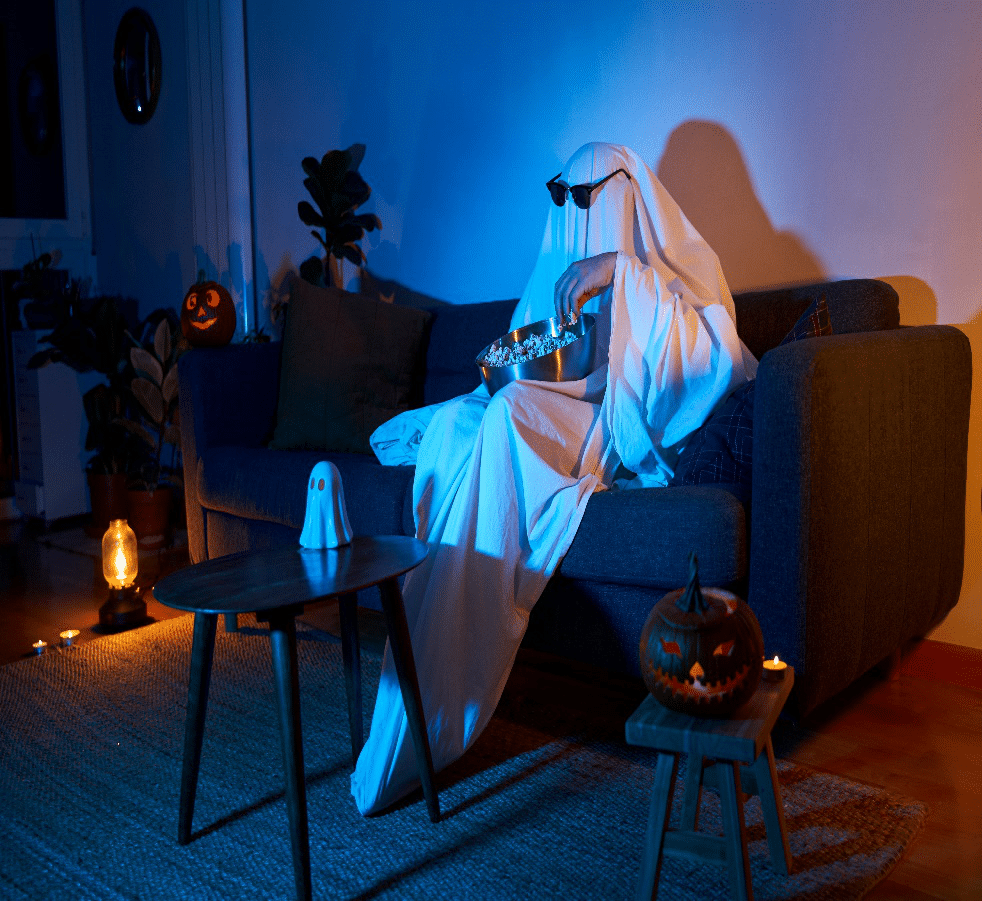 Person dressed as a ghost enjoying a scary movie night with themed decorations and props.