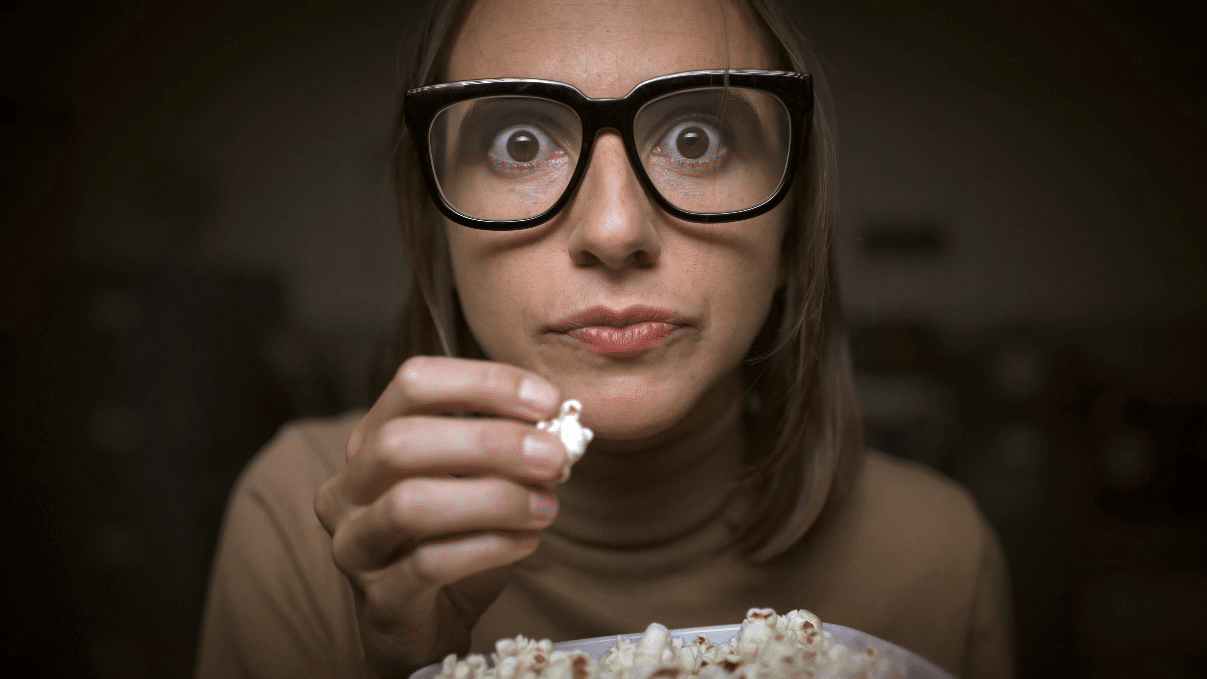 Woman enjoying a movie while eating popcorn in a dimly lit theater.